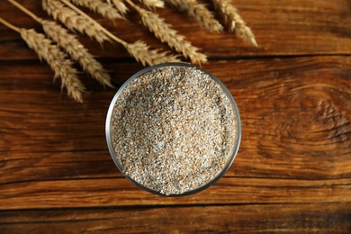 Photo of Fresh rye bran in bowl and spikelets on wooden table, flat lay