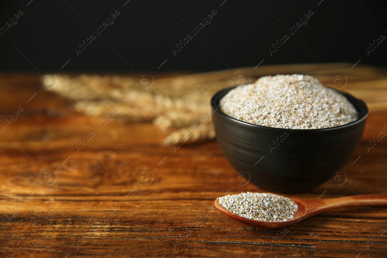 Photo of Fresh rye bran in bowl and spoon on wooden table, closeup. Space for text