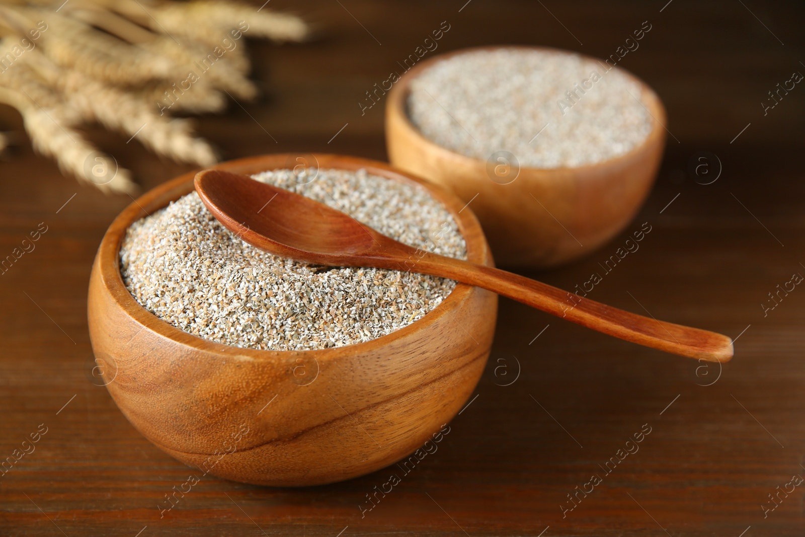 Photo of Fresh rye bran in bowls and spoon on wooden table, closeup