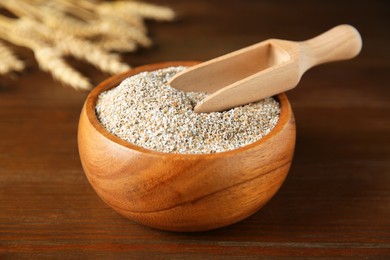 Photo of Fresh rye bran in bowl and scoop on wooden table, closeup