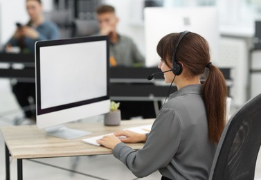 Photo of Saleswoman talking to client via headset at desk in office