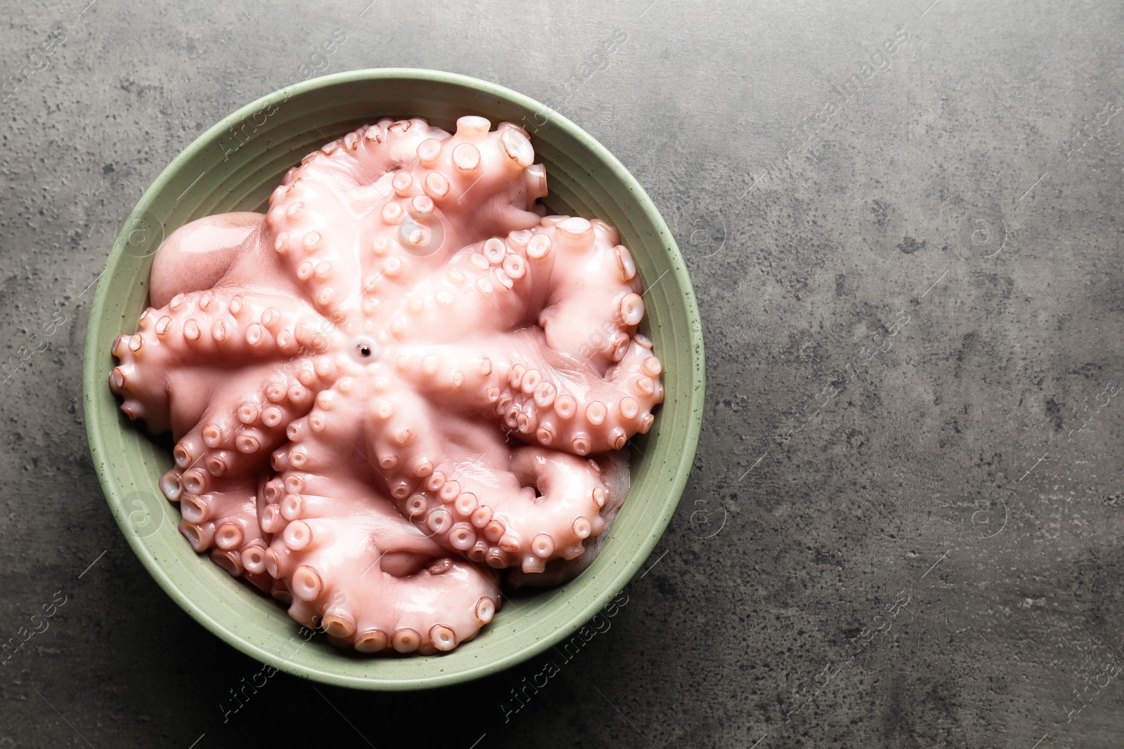 Photo of Raw octopus in bowl on grey textured table, top view. Space for text