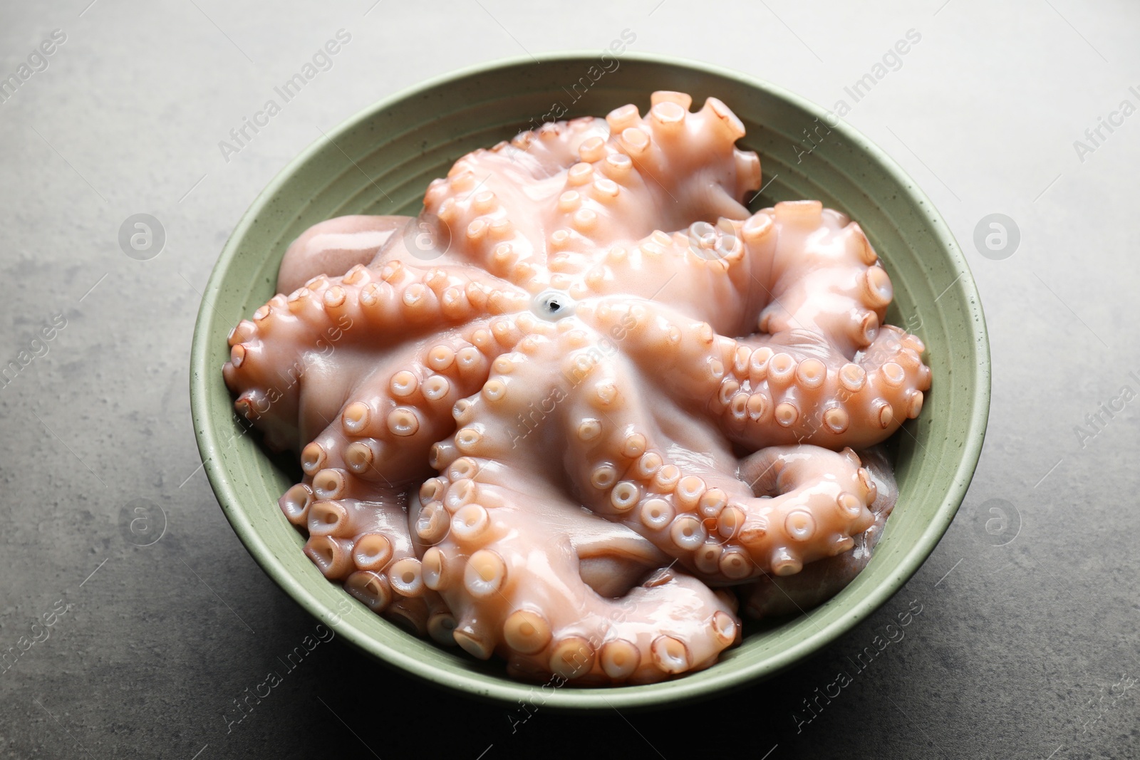 Photo of Raw octopus in bowl on grey textured table, closeup