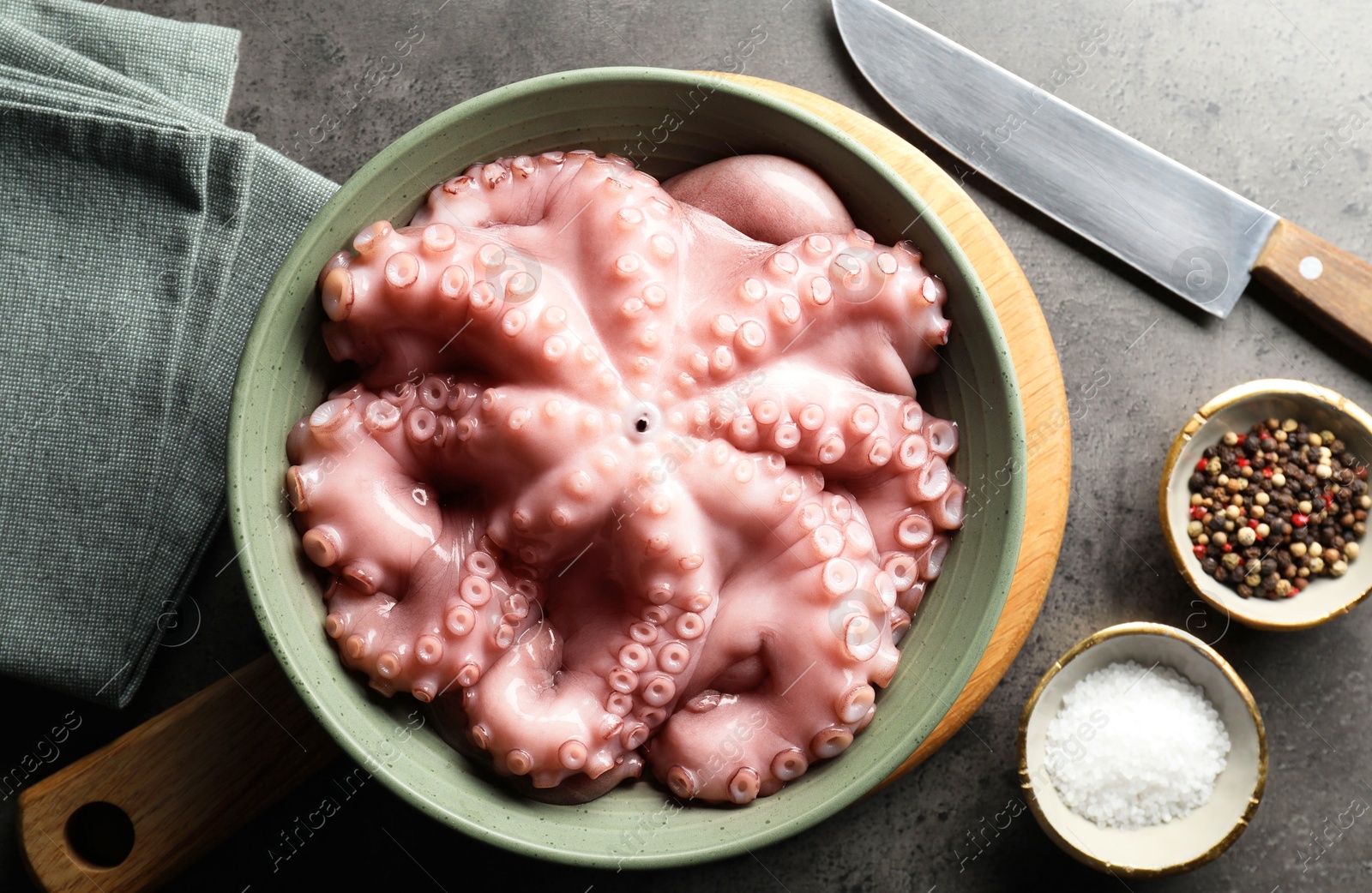 Photo of Raw octopus in bowl, peppercorns and salt on grey textured table, flat lay