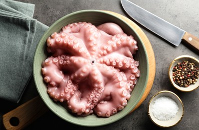 Photo of Raw octopus in bowl, peppercorns and salt on grey textured table, flat lay