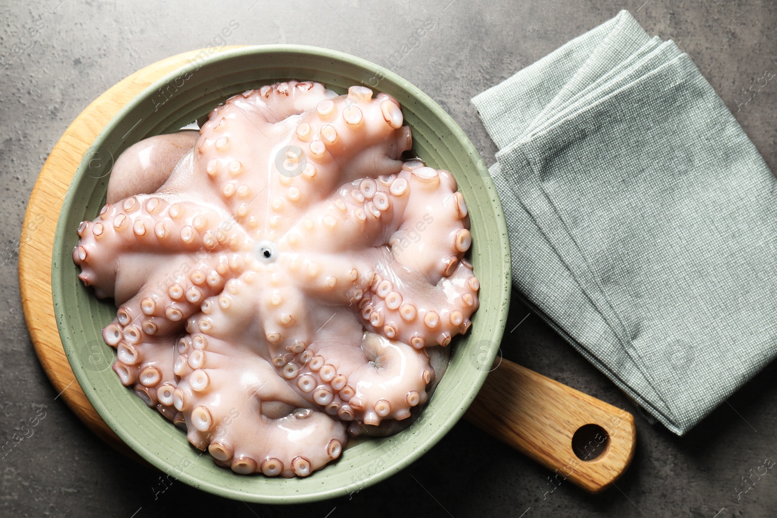 Photo of Raw octopus in bowl and napkin on grey textured table, flat lay