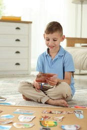 Photo of Creating vision board. Little boy cutting out picture on floor at home