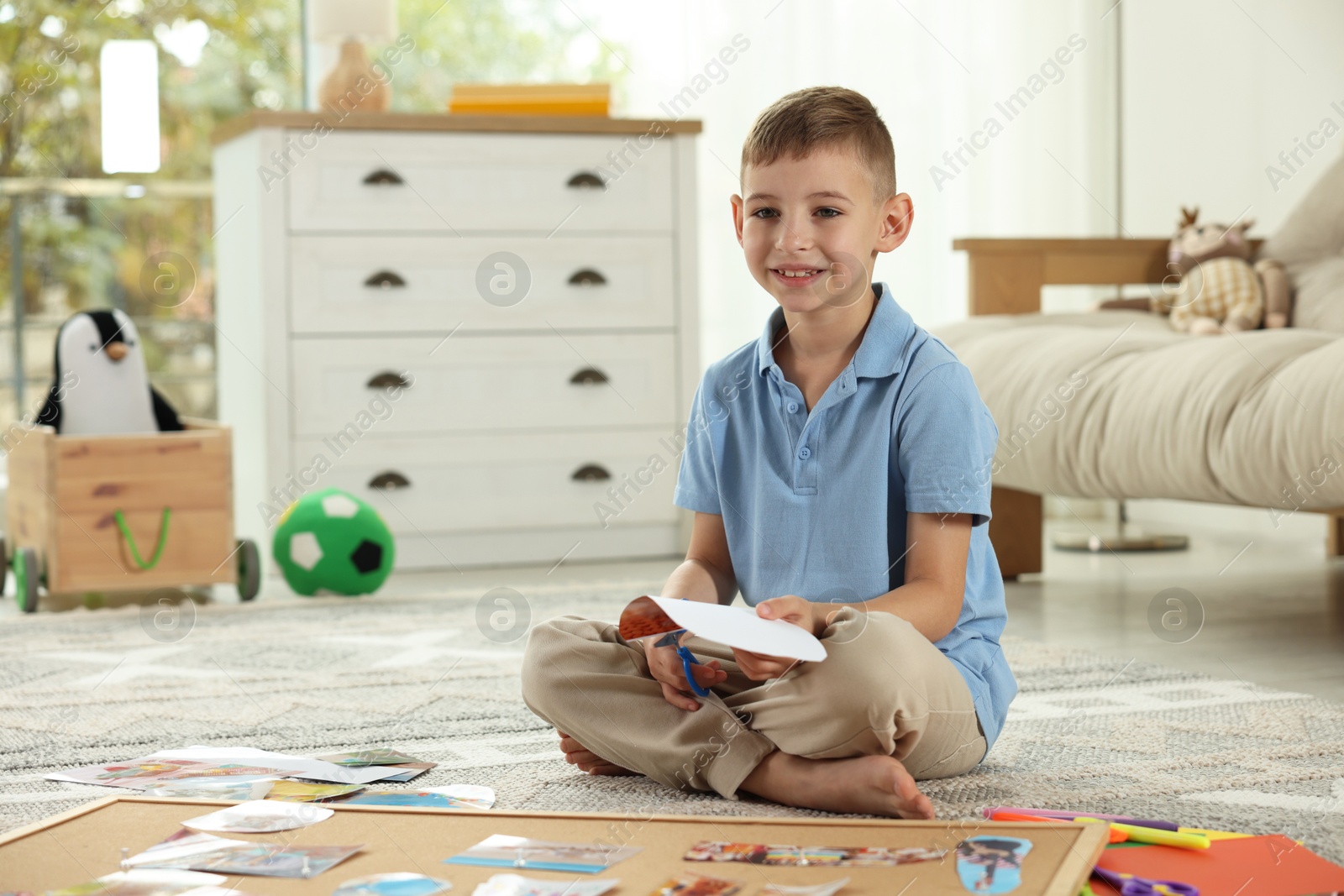 Photo of Creating vision board. Little boy cutting out picture on floor at home