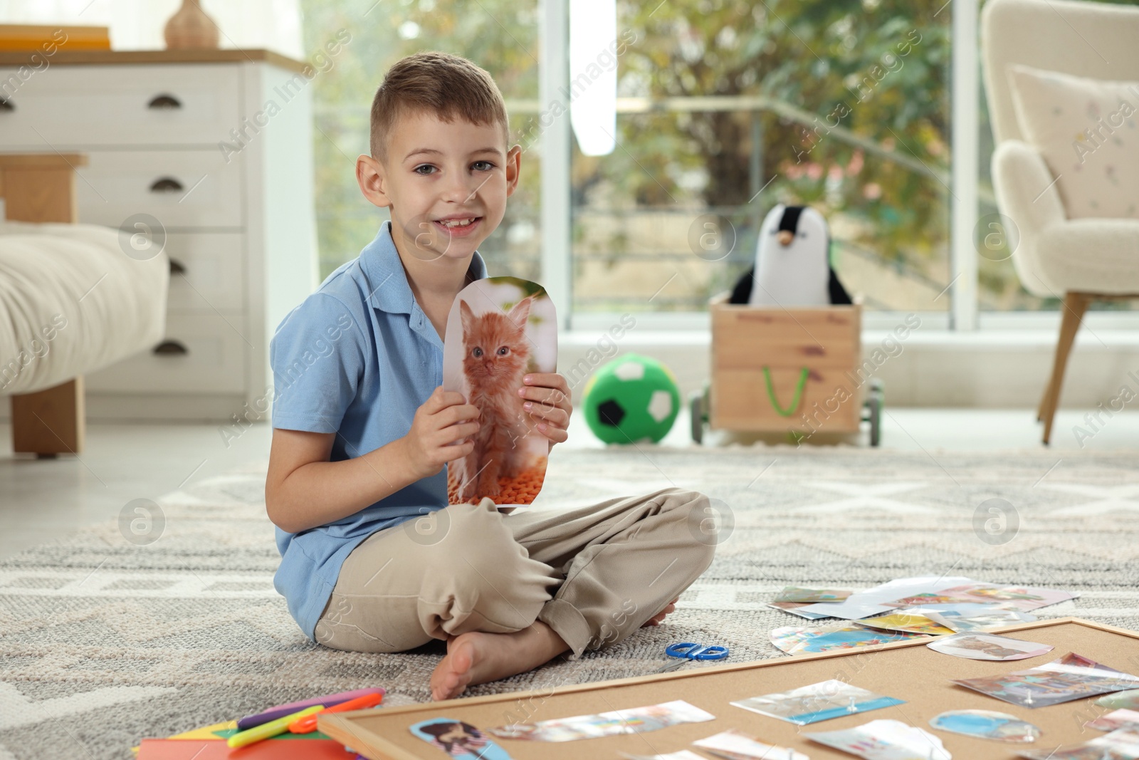 Photo of Creating vision board. Little boy with picture of cat on floor indoors