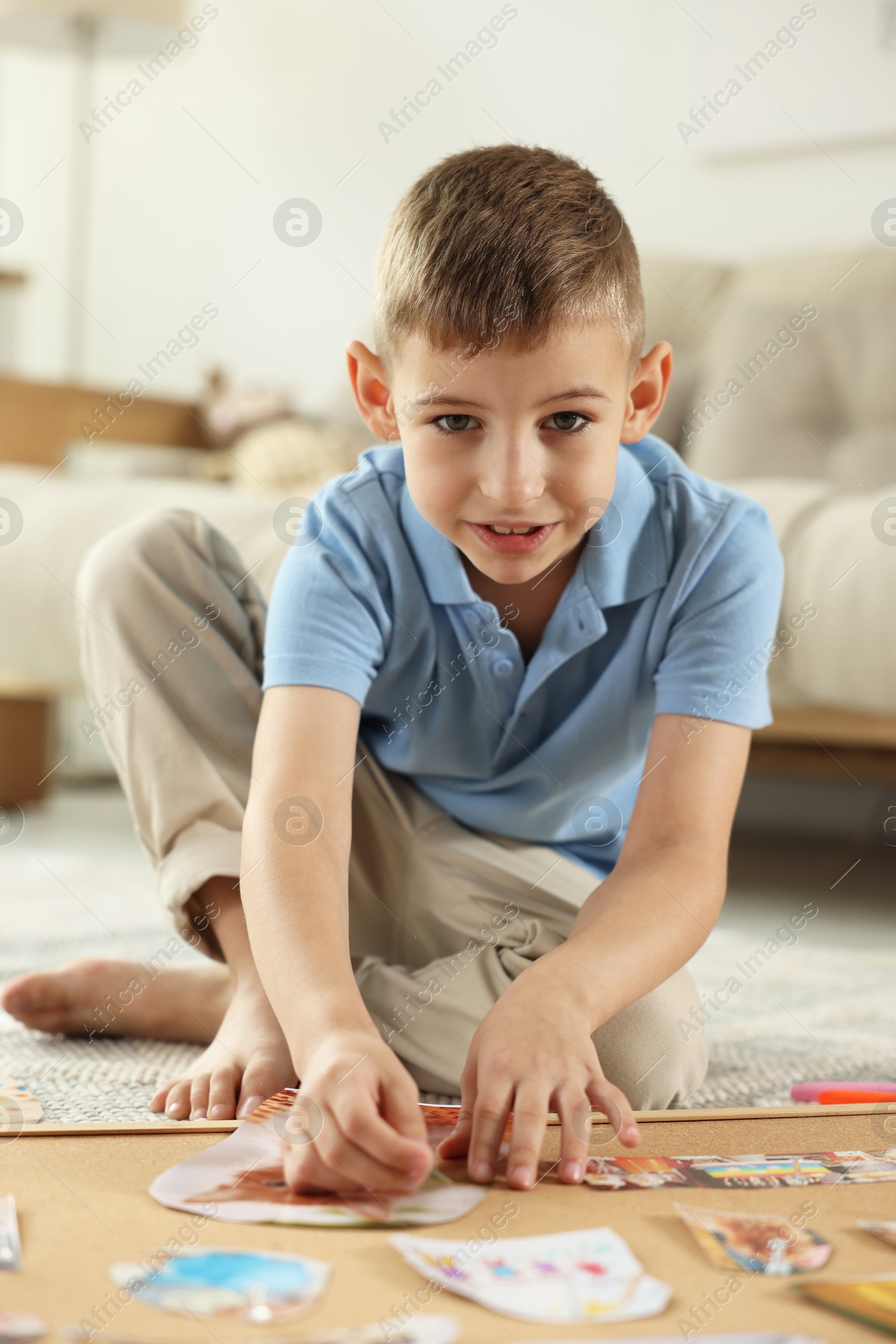 Photo of Little boy creating vision board with different pictures and other elements on floor at home