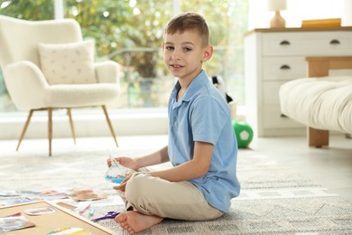 Photo of Creating vision board. Little boy with picture of cupcake on floor indoors