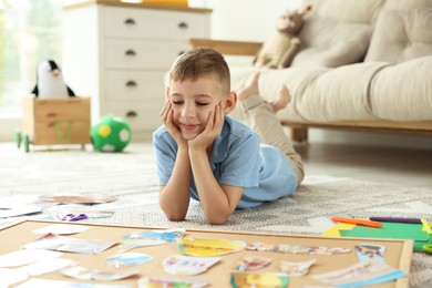 Little boy near vision board with different pictures and other elements on floor indoors