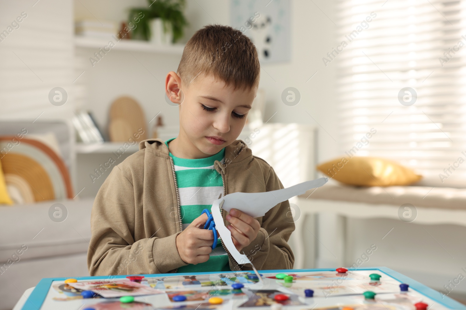 Photo of Creating vision board. Little boy cutting out picture at table indoors