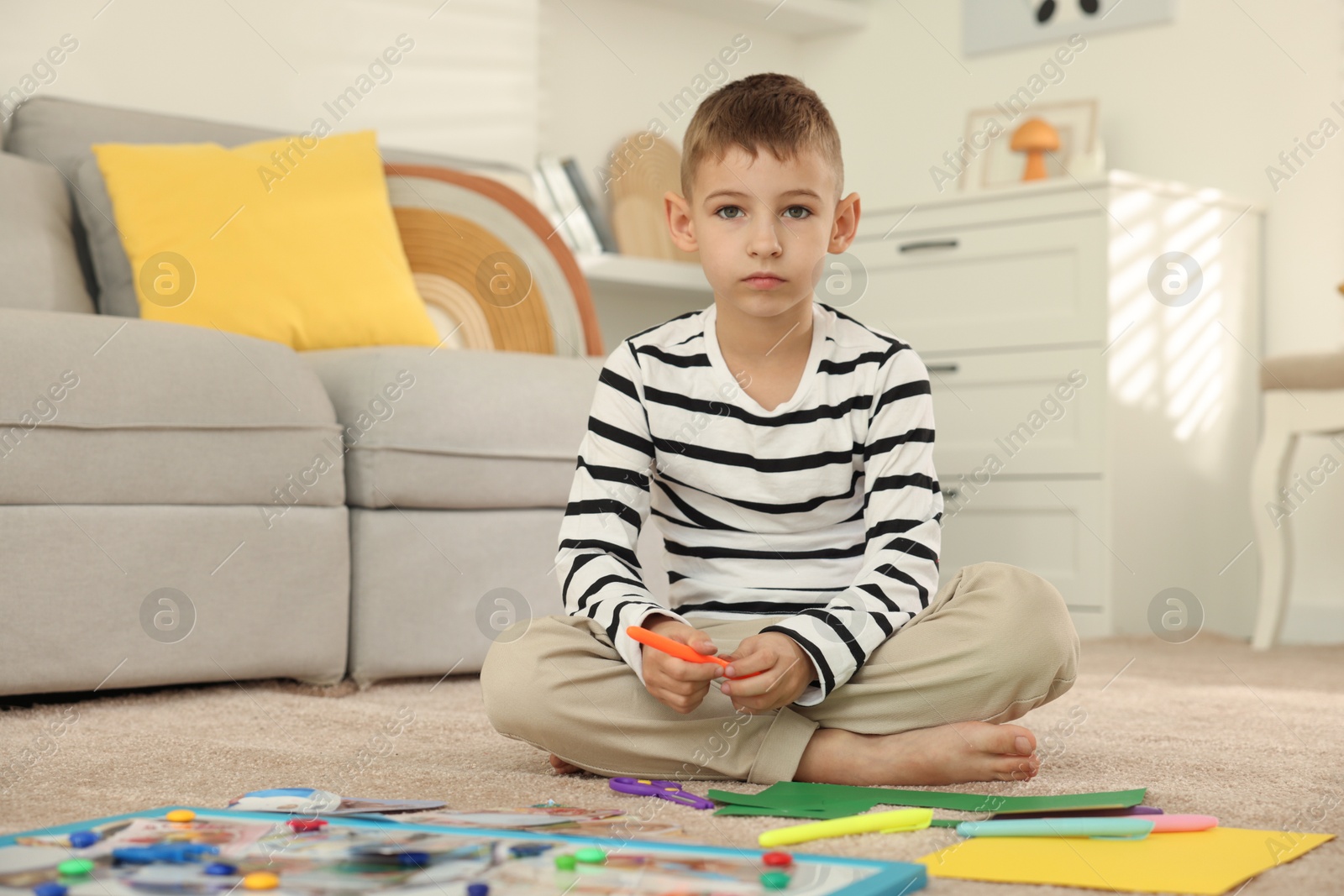 Photo of Little boy creating vision board with different pictures and other elements on floor at home