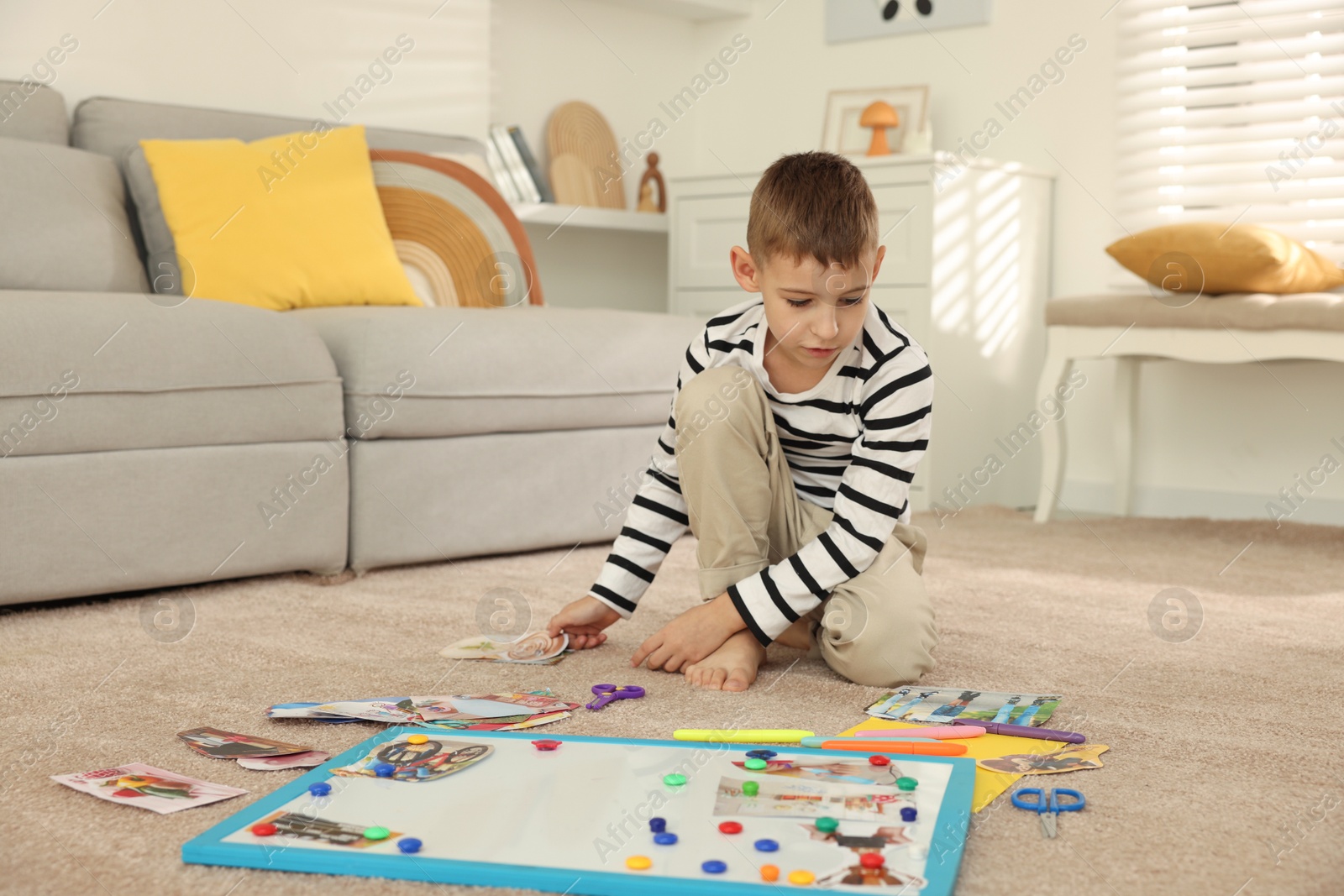 Photo of Little boy creating vision board with different pictures and other elements on floor at home