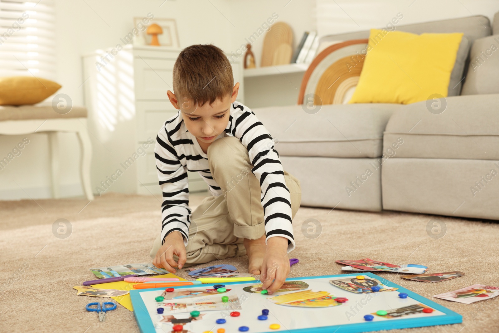 Photo of Little boy creating vision board with different pictures and other elements on floor at home