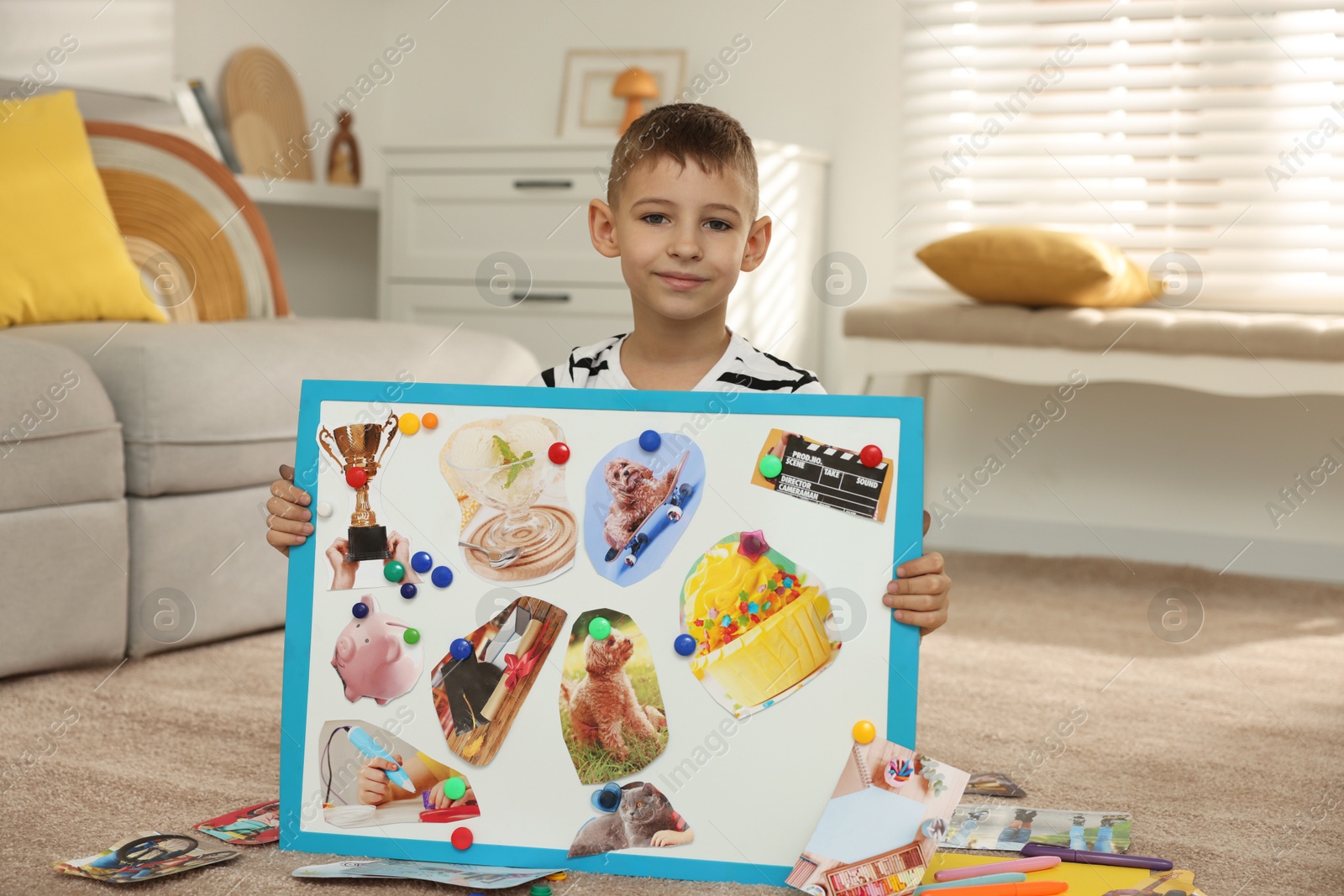 Photo of Little boy holding vision board with different pictures on floor at home