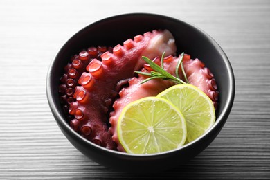 Photo of Fresh raw octopus, lemon and rosemary in bowl on dark textured table, closeup