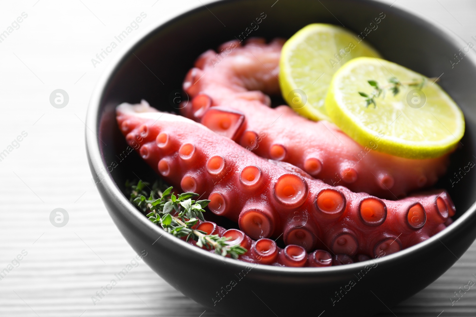 Photo of Fresh raw octopus, lemon and thyme in bowl on table, closeup