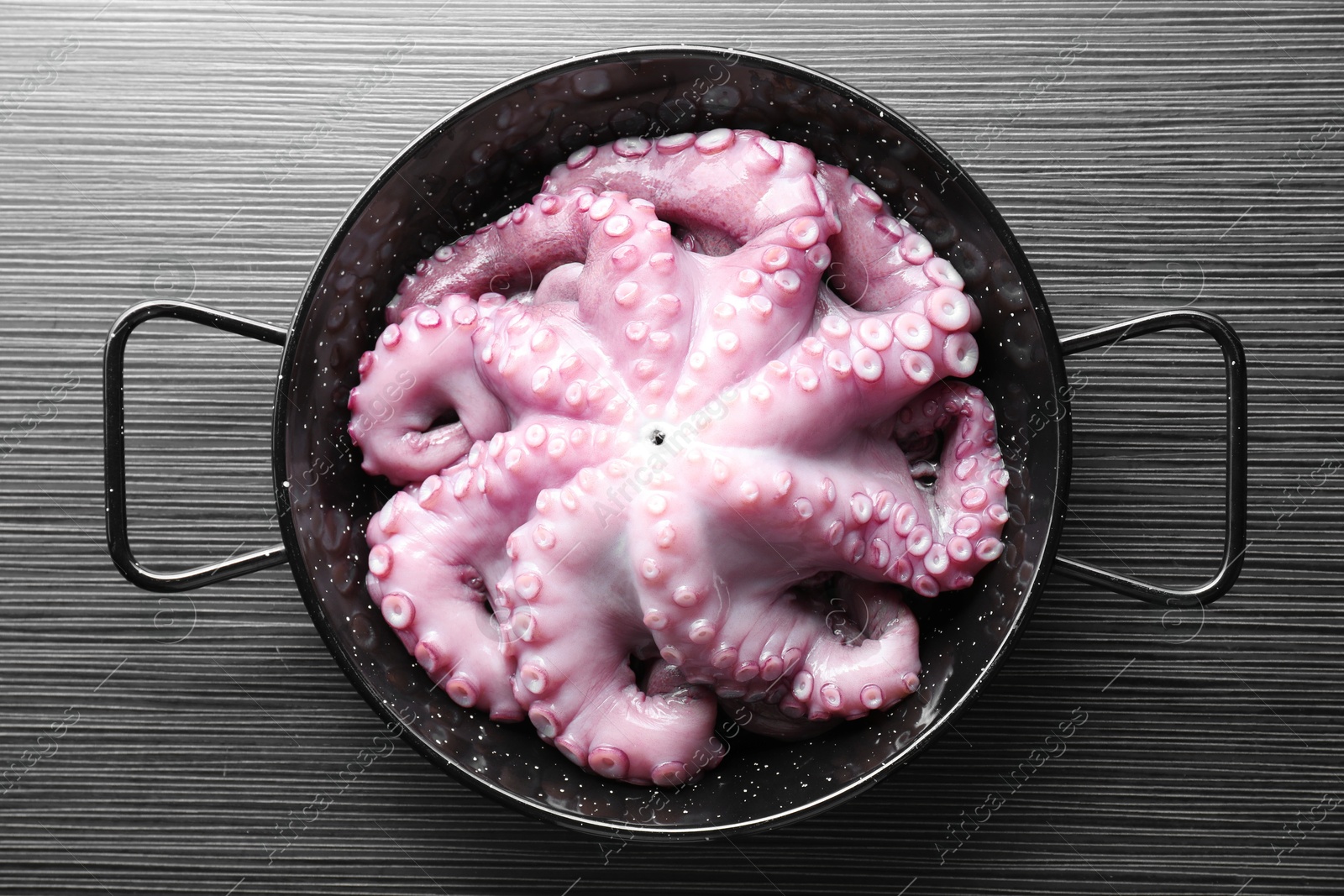 Photo of Fresh raw octopus in frying pan on dark textured table, top view