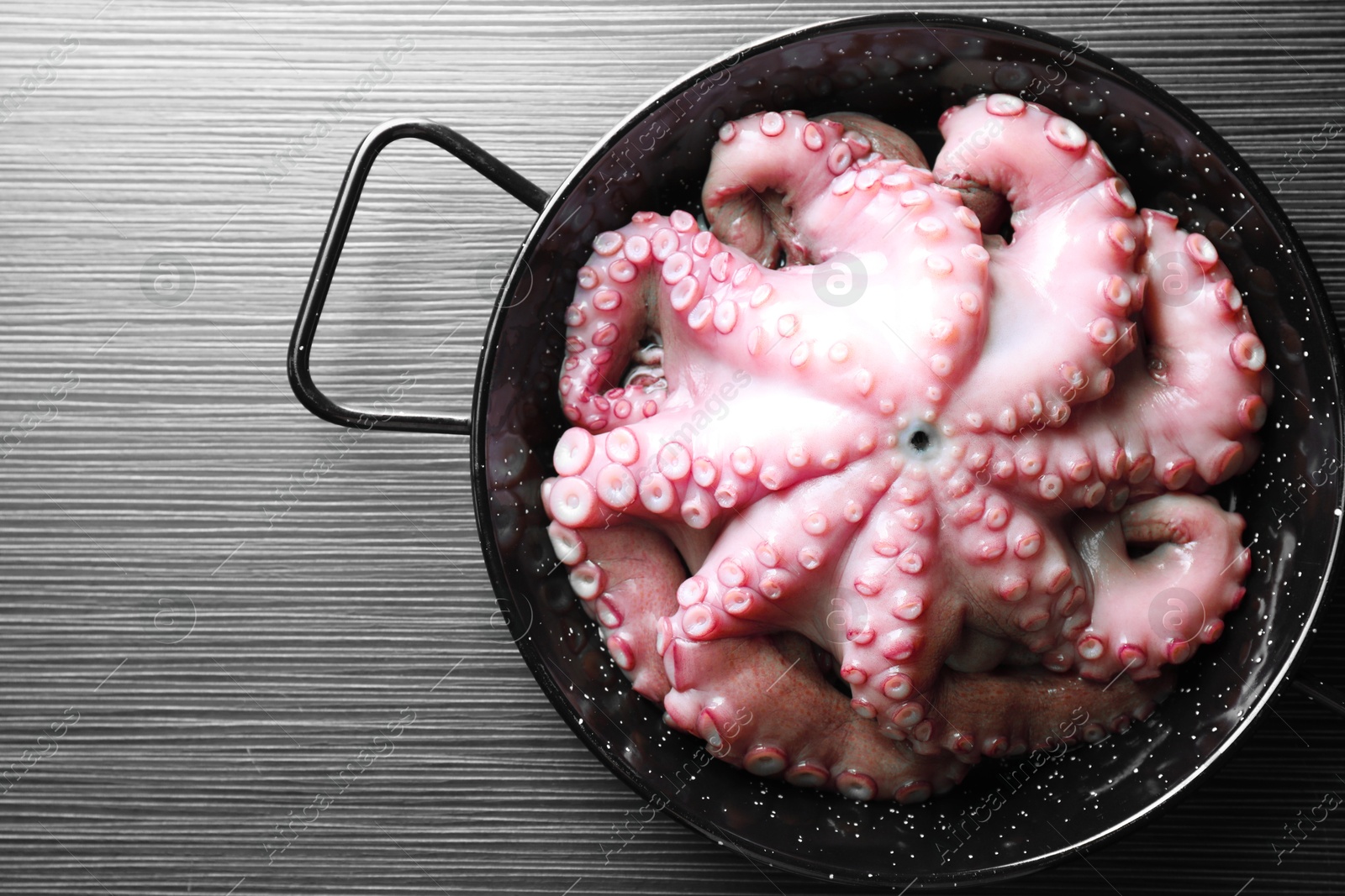 Photo of Fresh raw octopus in frying pan on dark textured table, top view