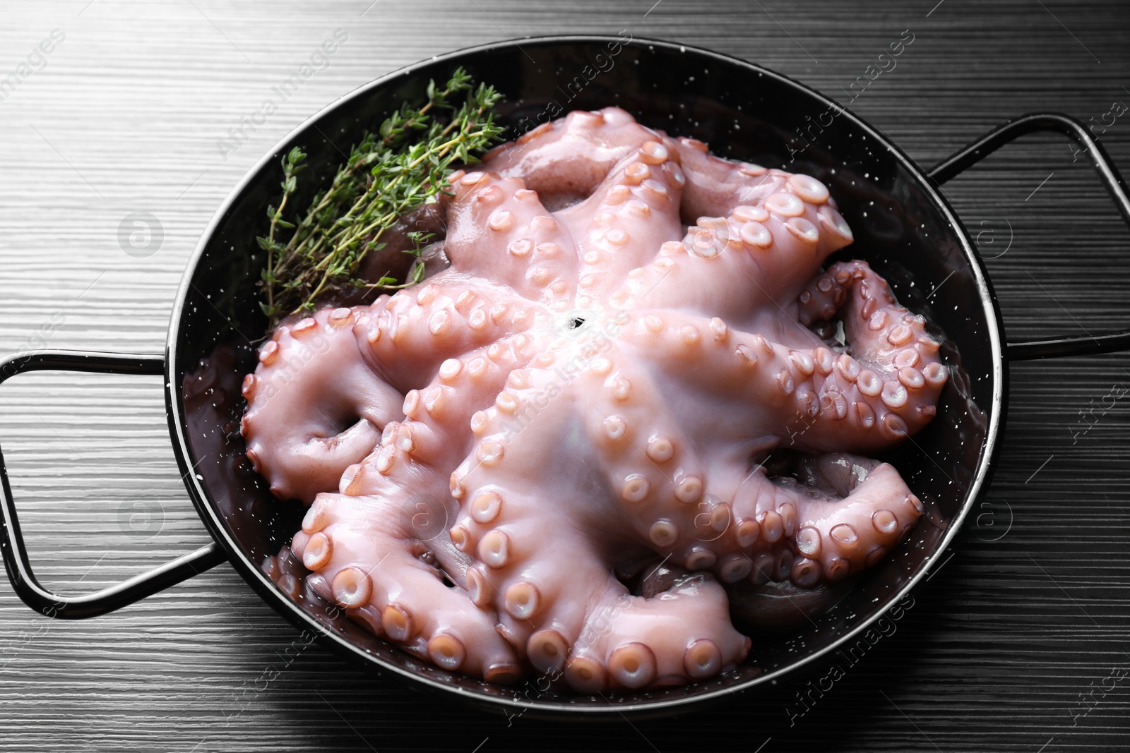 Photo of Fresh raw octopus and thyme in frying pan on dark textured table, closeup