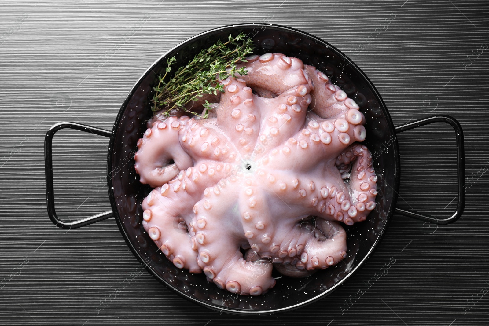 Photo of Fresh raw octopus and thyme in frying pan on dark textured table, top view