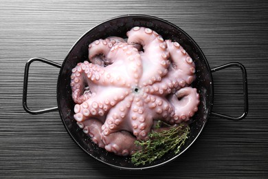 Photo of Fresh raw octopus and thyme in frying pan on dark textured table, top view