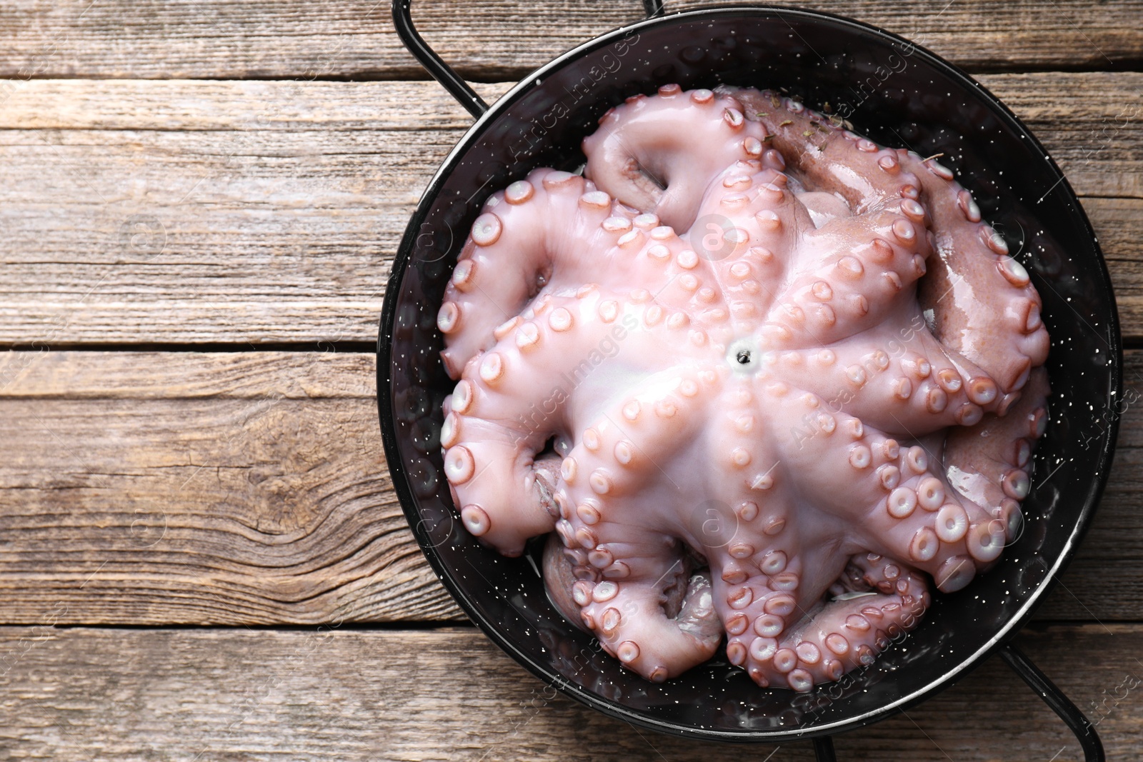 Photo of Fresh raw octopus in frying pan on wooden table, top view. Space for text