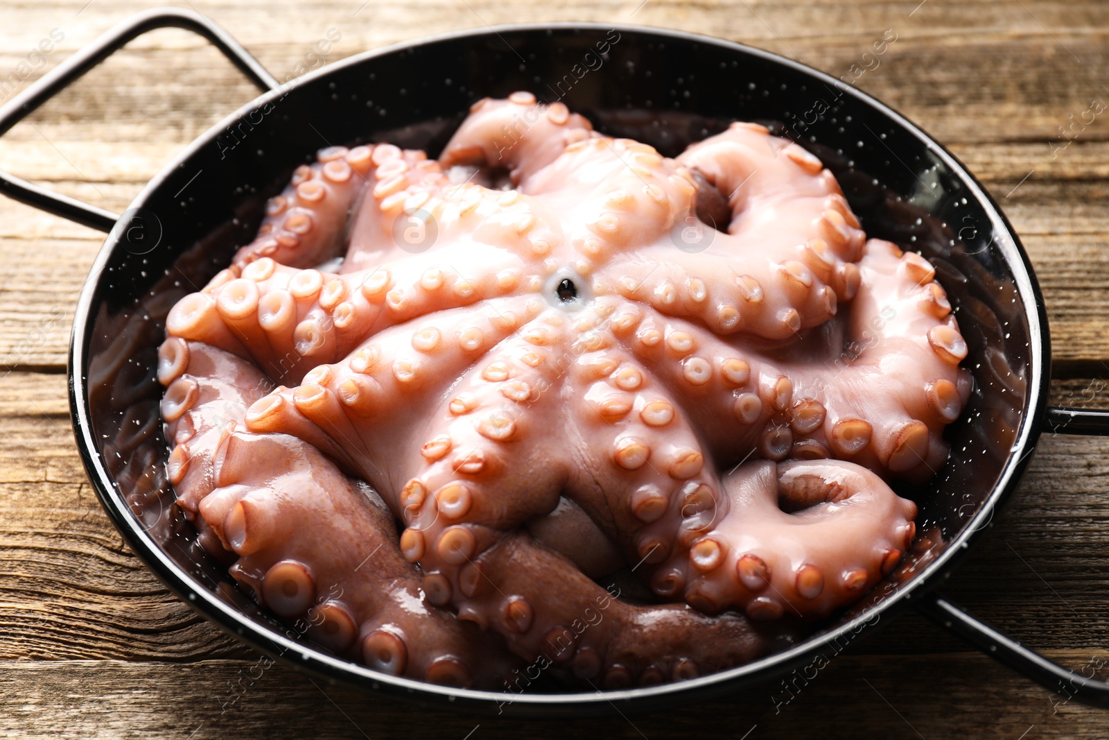 Photo of Fresh raw octopus in frying pan on wooden table, closeup