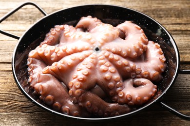 Fresh raw octopus in frying pan on wooden table, closeup