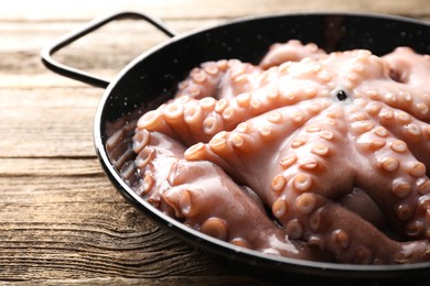 Photo of Fresh raw octopus in frying pan on wooden table, closeup