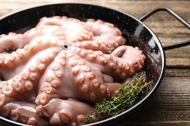 Photo of Fresh raw octopus and thyme in frying pan on wooden table, closeup