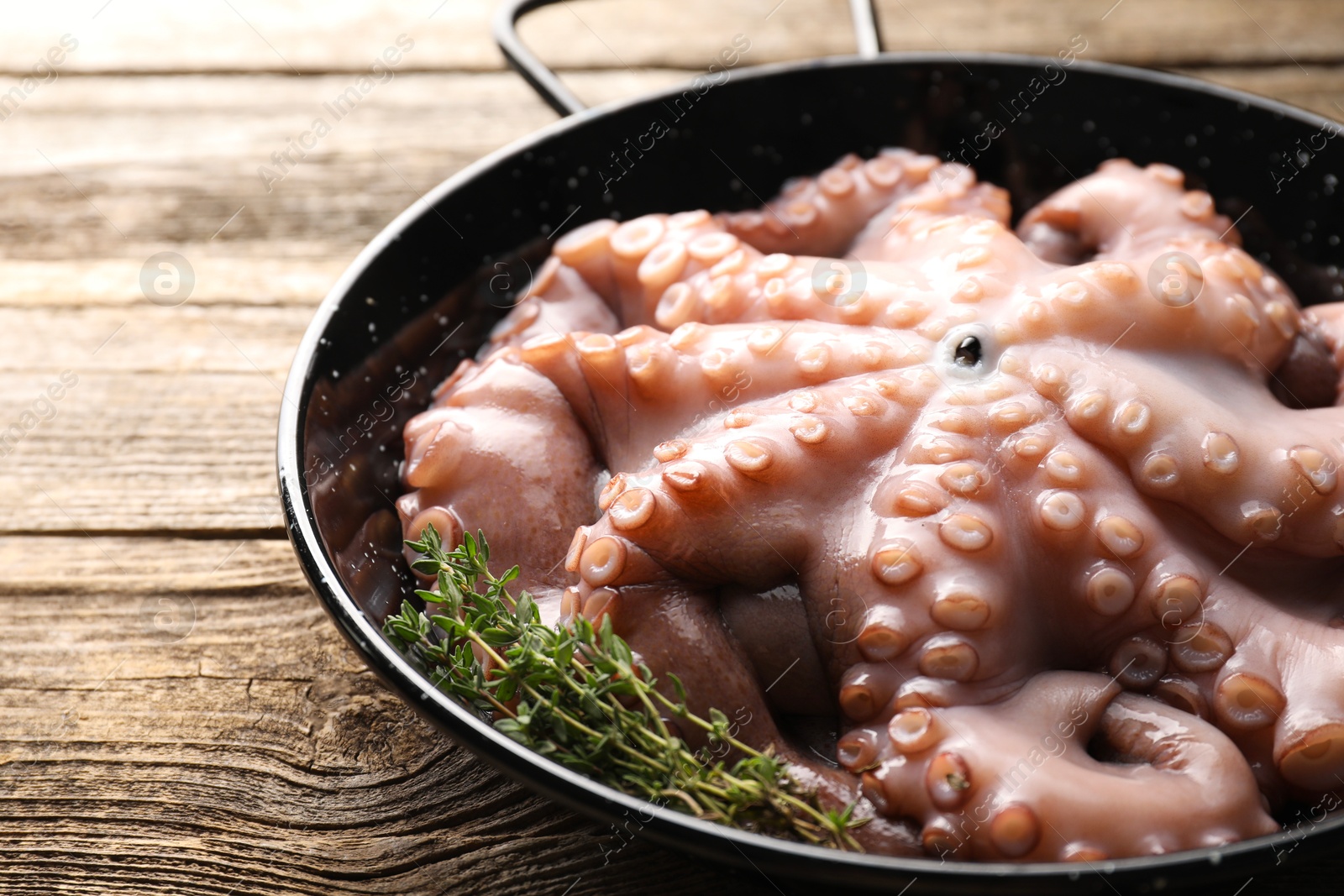 Photo of Fresh raw octopus and thyme in frying pan on wooden table, closeup