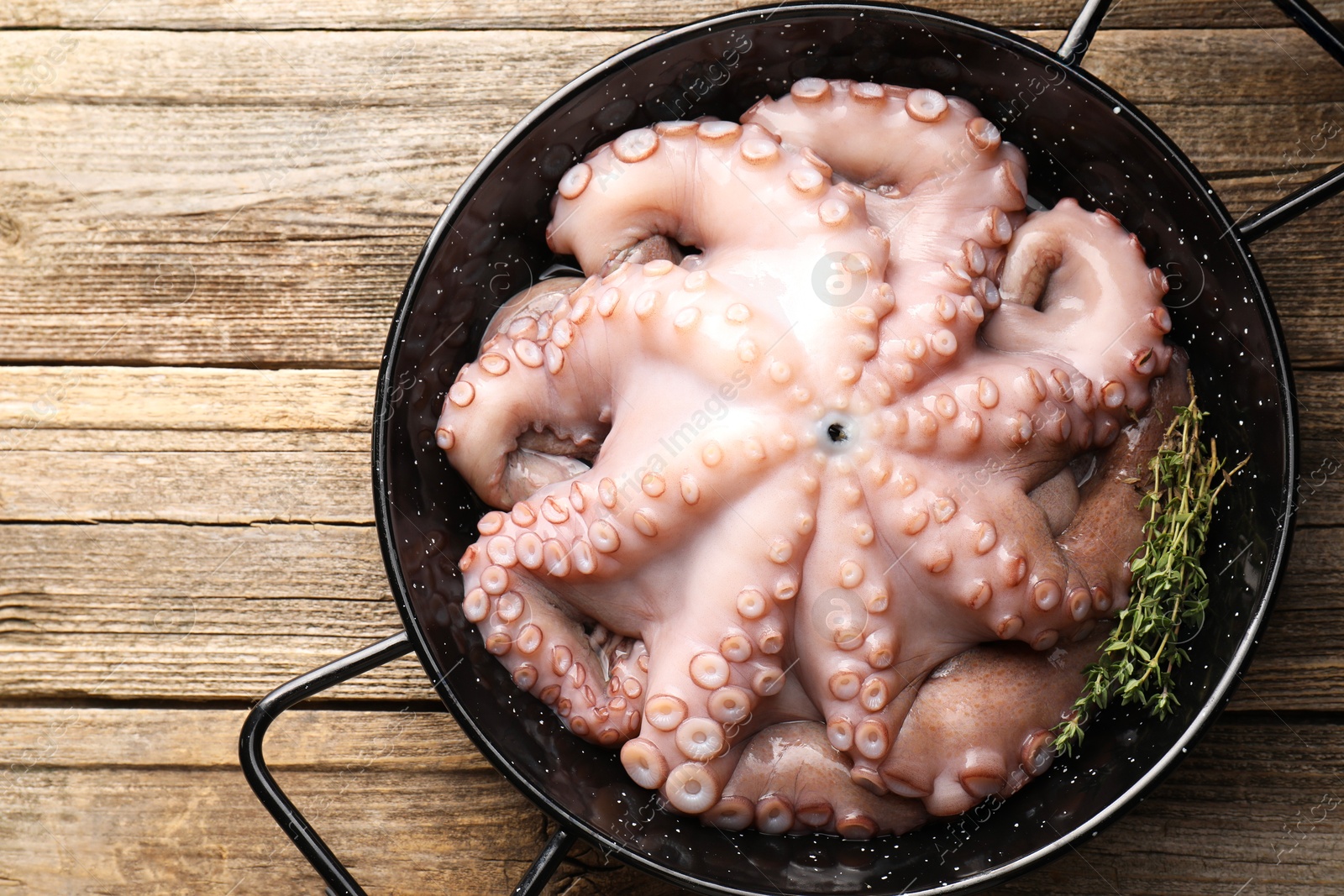 Photo of Fresh raw octopus and thyme in frying pan on wooden table, top view