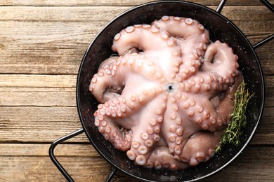 Photo of Fresh raw octopus and thyme in frying pan on wooden table, top view