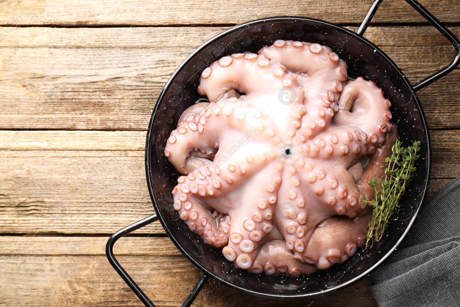 Photo of Fresh raw octopus and thyme in frying pan on wooden table, top view. Space for text