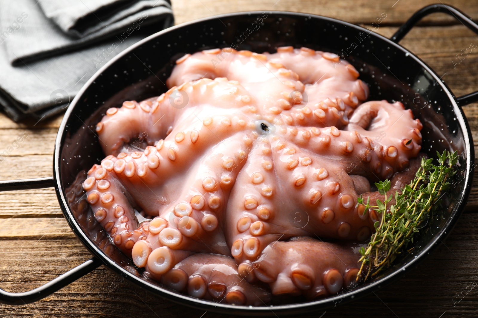 Photo of Fresh raw octopus and thyme in frying pan on wooden table, closeup