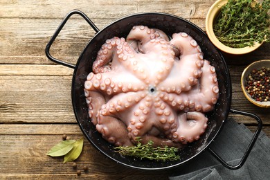 Photo of Fresh raw octopus and thyme in frying pan on wooden table, top view