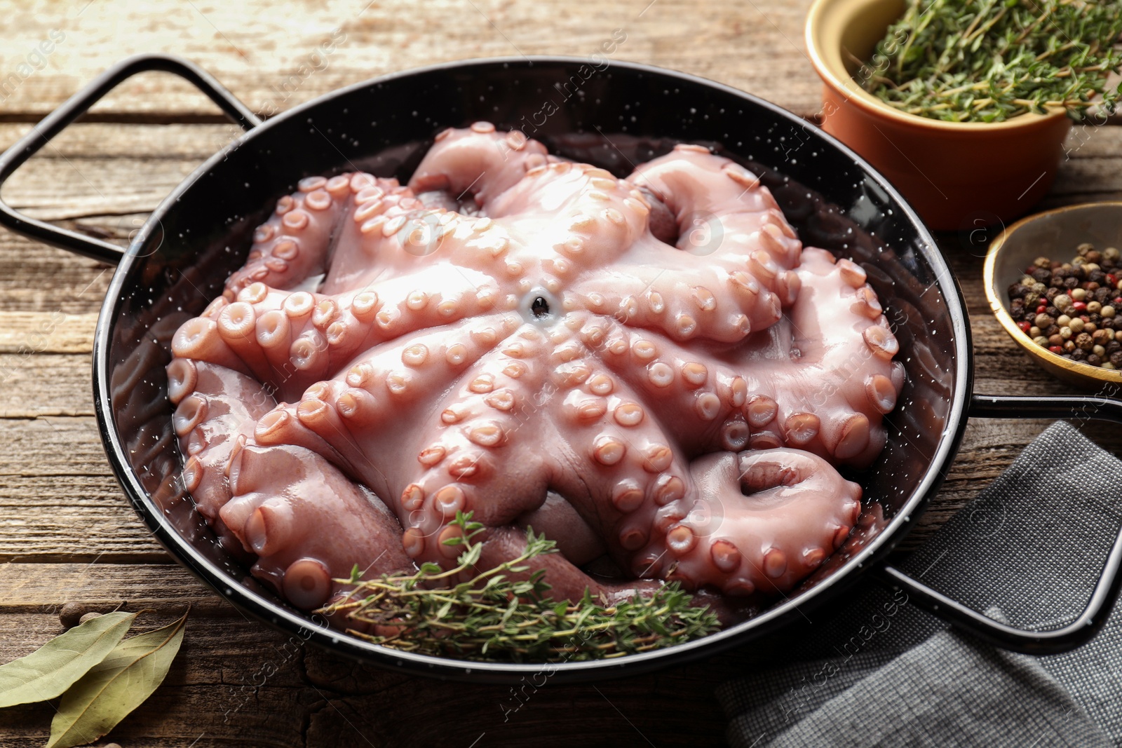 Photo of Fresh raw octopus and thyme in frying pan on wooden table, closeup