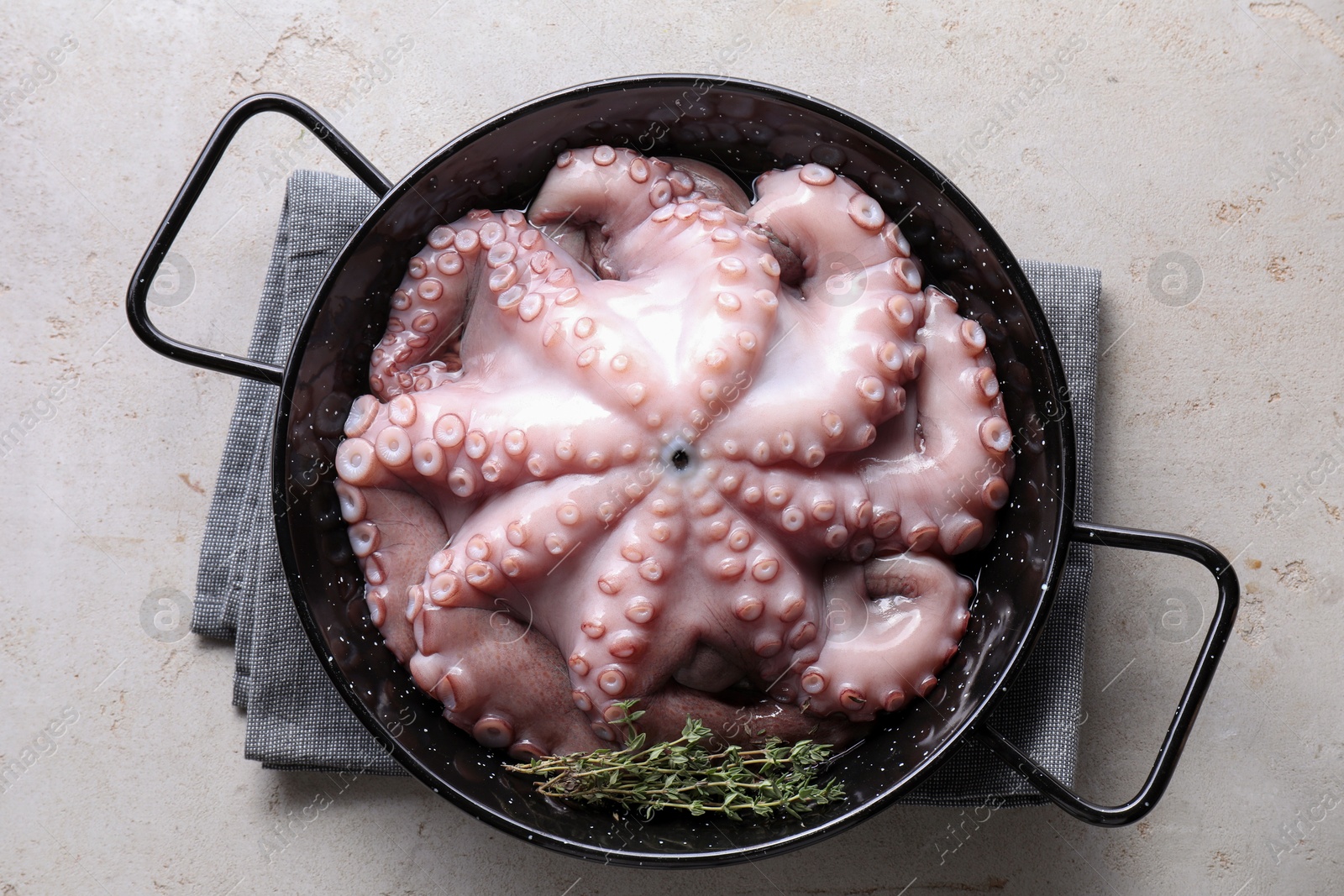 Photo of Fresh raw octopus and thyme in frying pan on grey table, top view