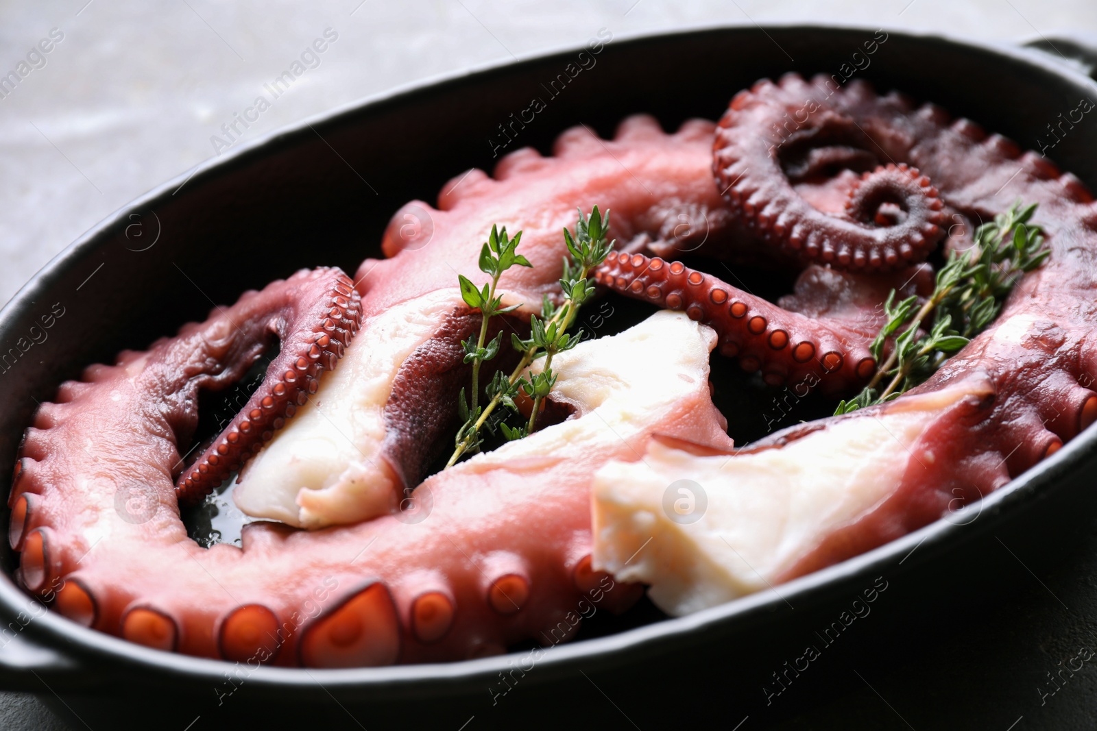 Photo of Fresh raw octopus and thyme in baking dish on table, closeup