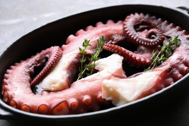 Photo of Fresh raw octopus and thyme in baking dish on table, closeup