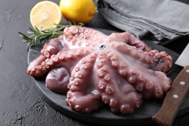 Photo of Fresh raw octopus, lemon, rosemary and knife on black table, closeup