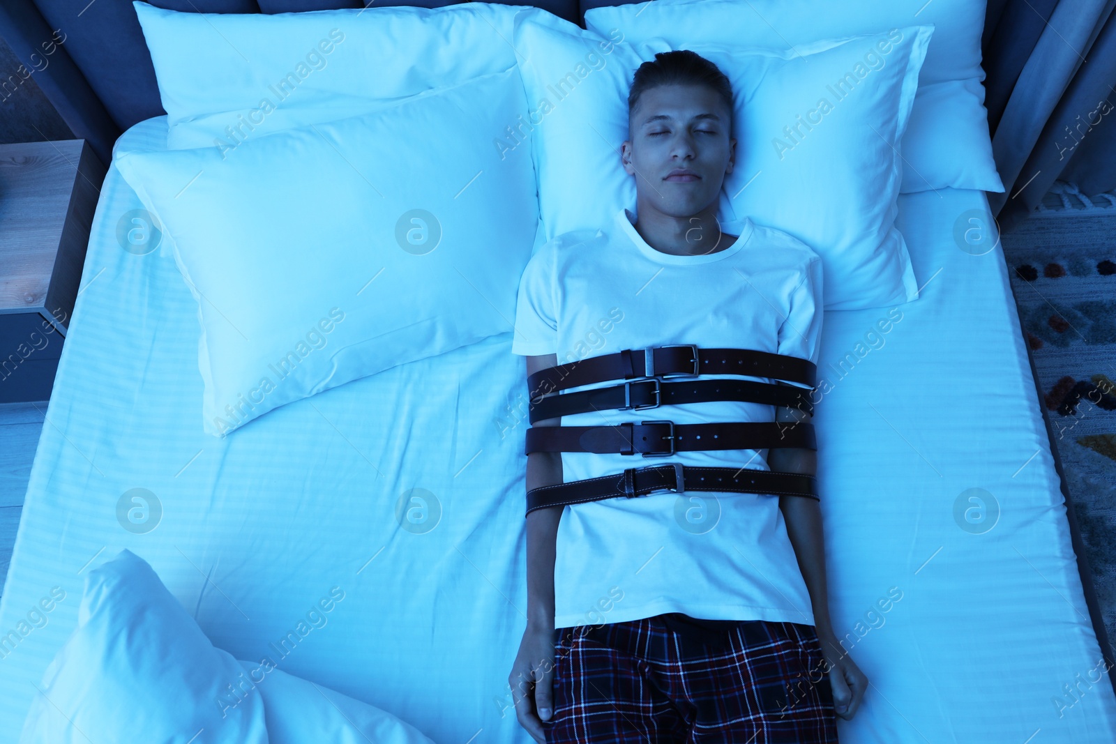 Photo of Sleepwalker fastened with belts lying on bed, above view