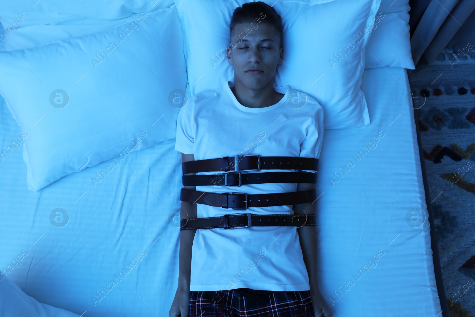 Photo of Sleepwalker fastened with belts lying on bed, top view