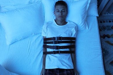 Photo of Sleepwalker fastened with belts lying on bed, top view