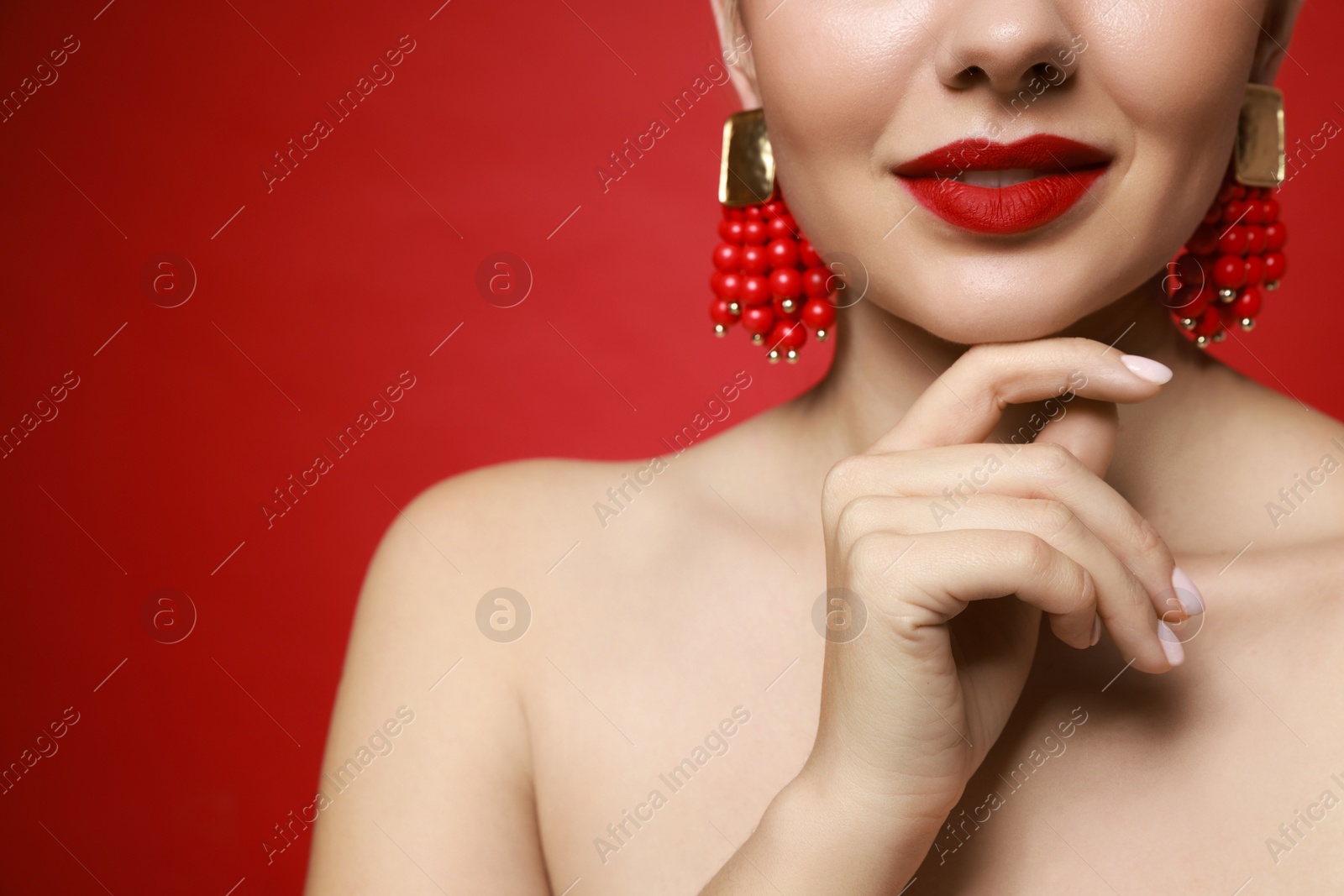 Photo of Beautiful young woman wearing elegant earrings on red background, closeup. Space for text