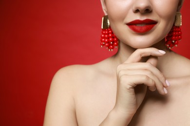 Beautiful young woman wearing elegant earrings on red background, closeup. Space for text