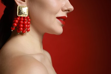 Photo of Beautiful young woman wearing elegant earrings on red background, closeup. Space for text